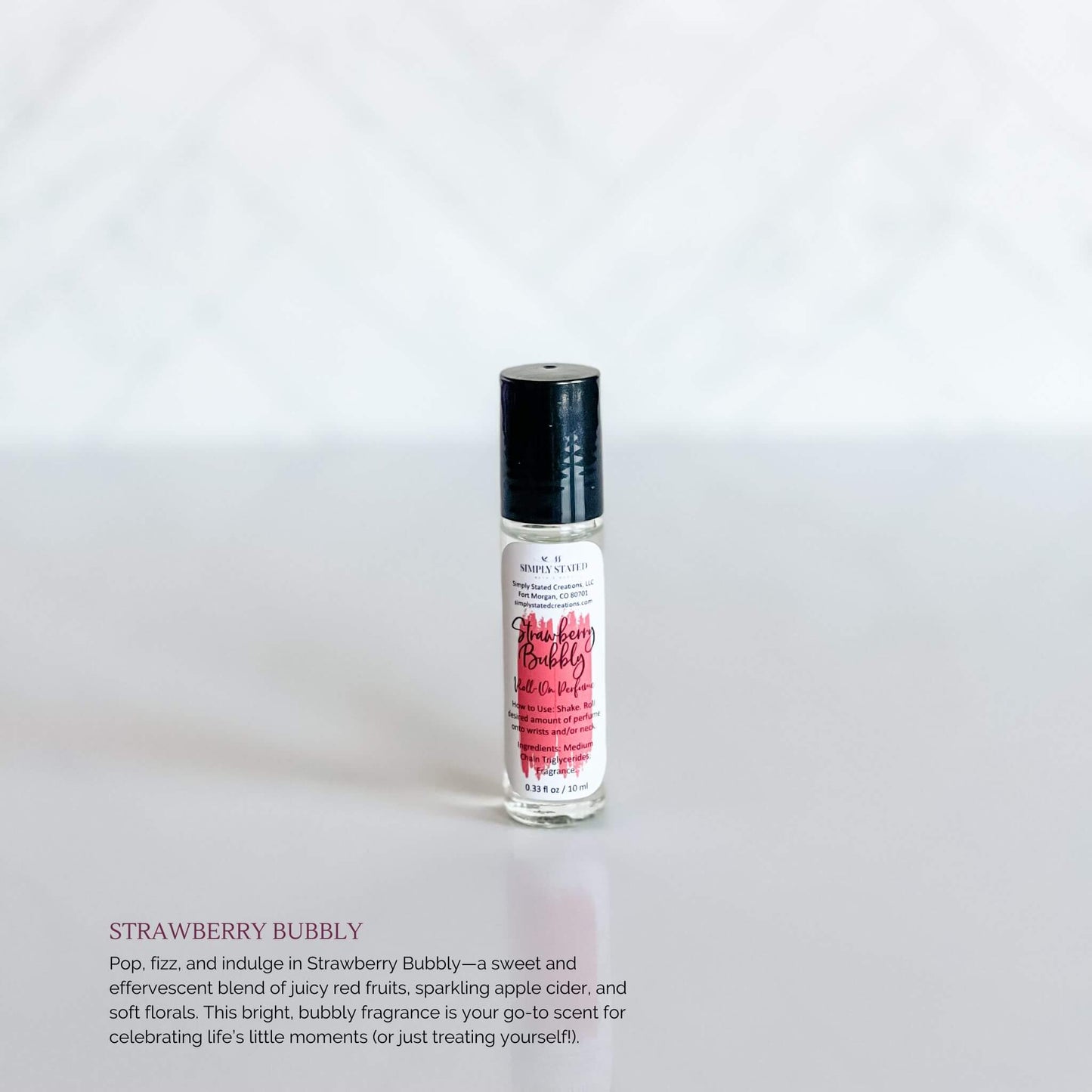 Simply Stated Bath & Body Strawberry Bubbly Roll-On Perfume in a clear glass bottle with a bright pink label and black cap, set against a white background.