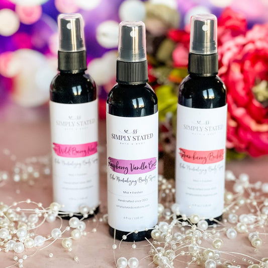 A trio of Sweet Temptations Body Sprays—Raspberry Vanilla Crush, Strawberry Bubbly, and Wild Berry Kiss—arranged with pearl accents and vibrant floral decor on a blush pink background.